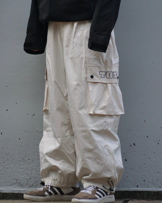 Person wearing white cargo pants with a black jacket and Adidas shoes against a gray wall.