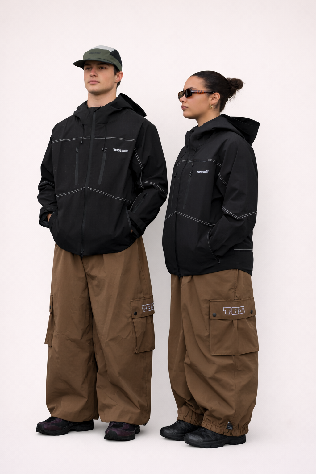 Two people wearing black jackets and brown pants on a white background