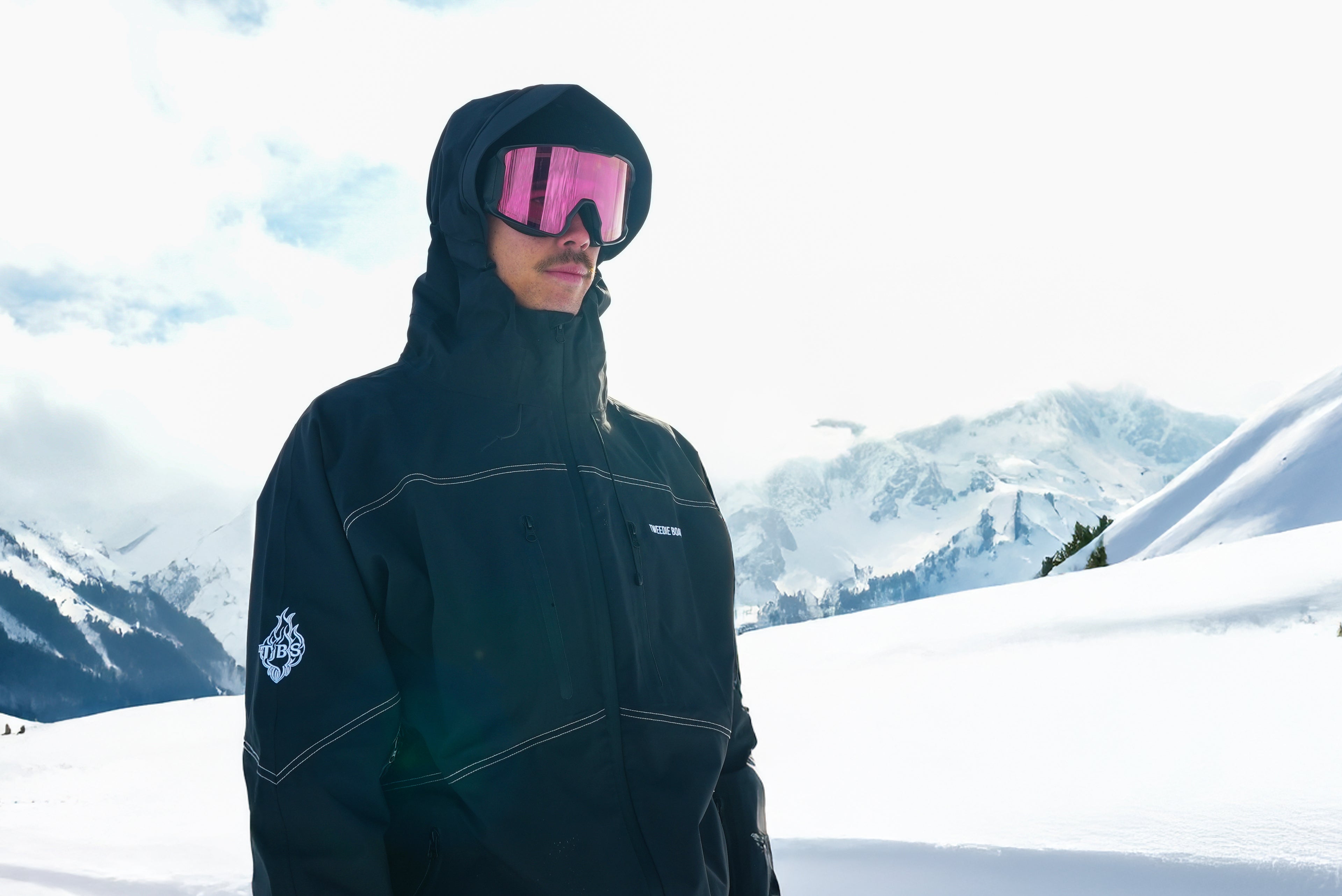 Person wearing a black jacket and pink goggles in a snowy mountain landscape