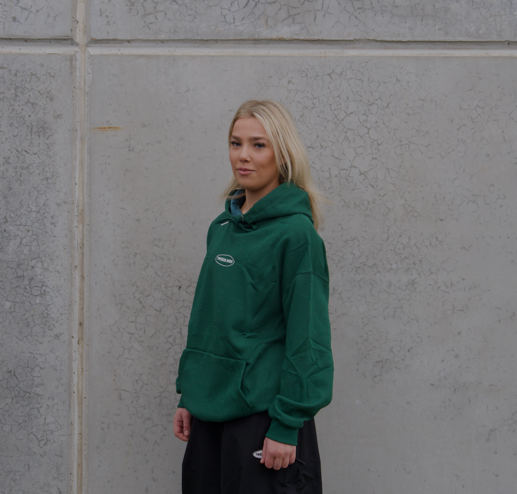 Person wearing a green hoodie standing against a gray wall