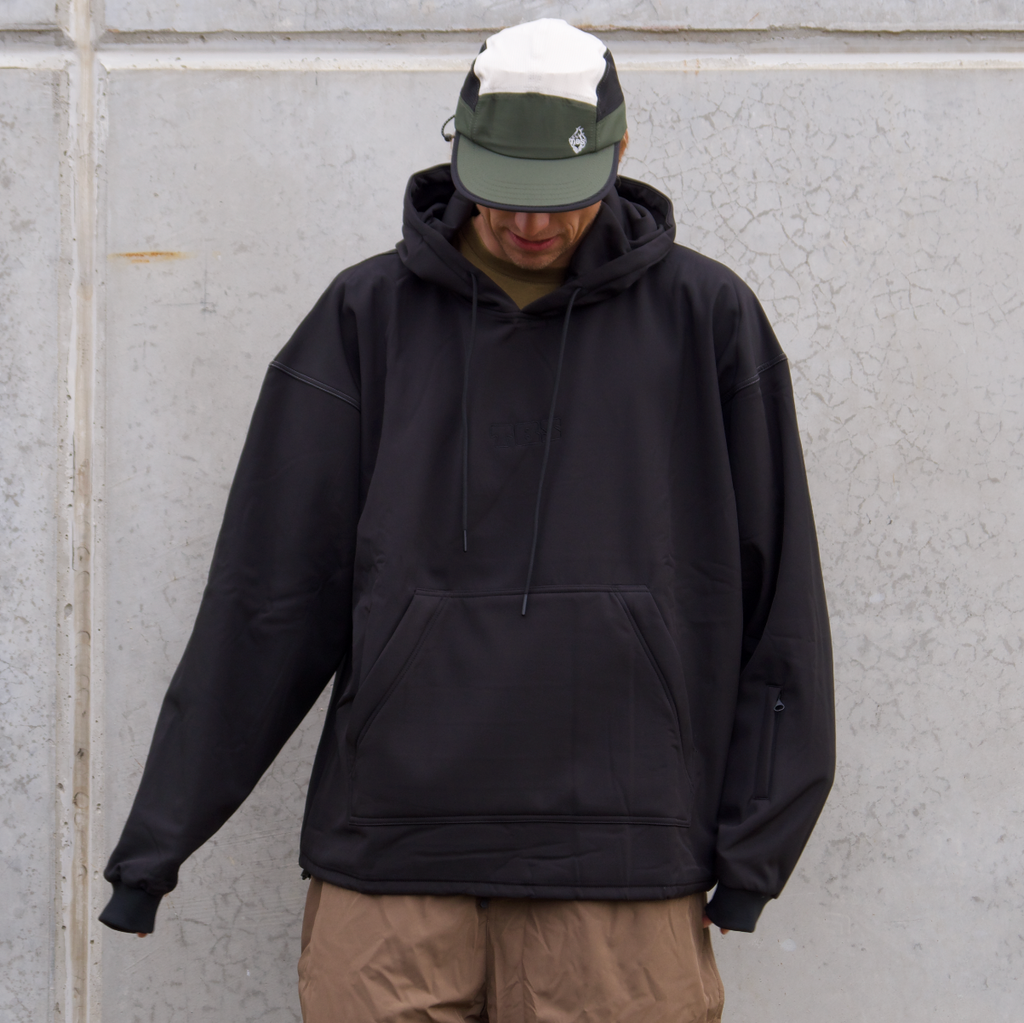 Person wearing a black hoodie and beige pants against a gray wall