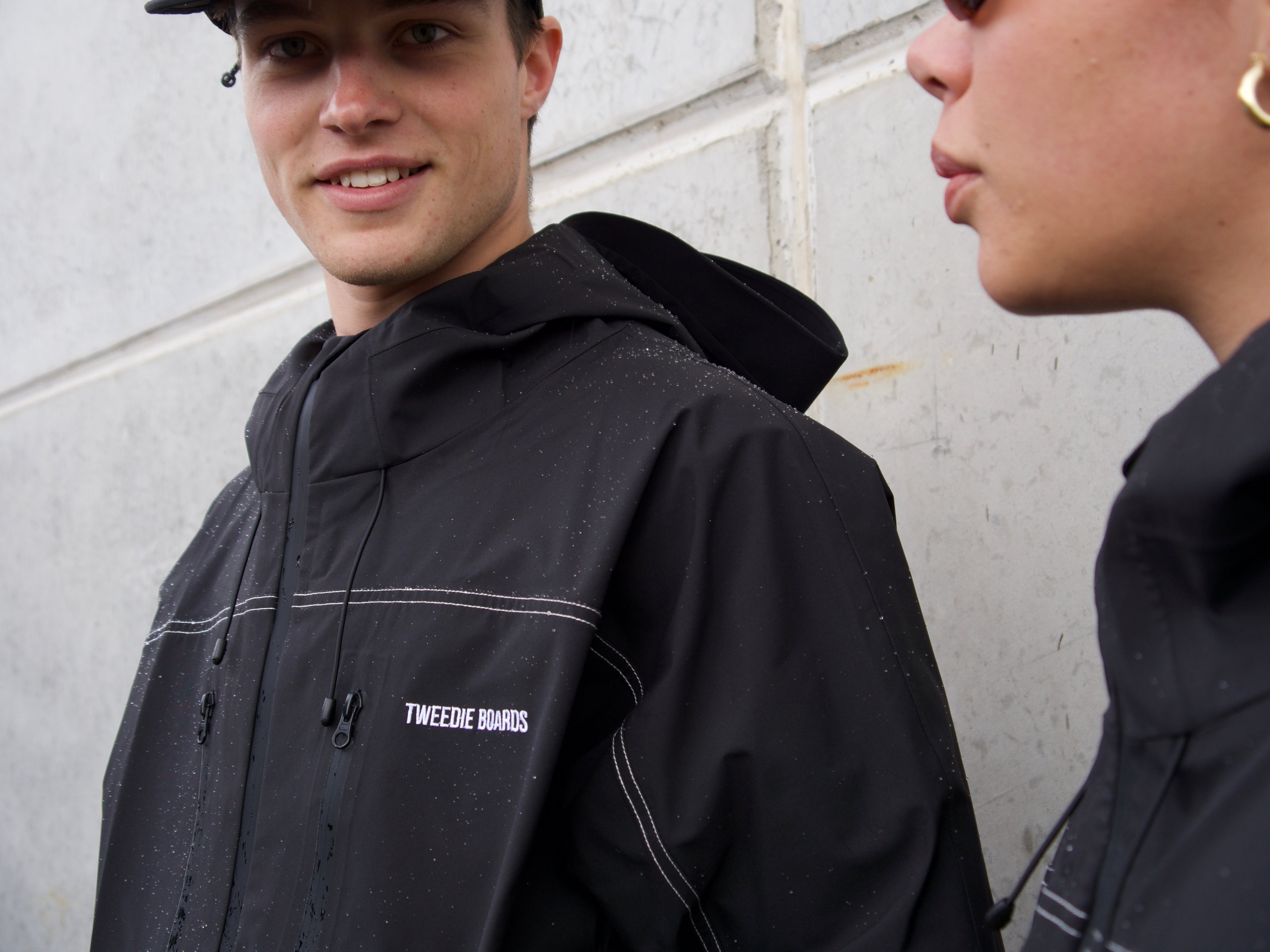 Person wearing a black jacket with 'Tweeide Boards' branding against a light-colored wall.